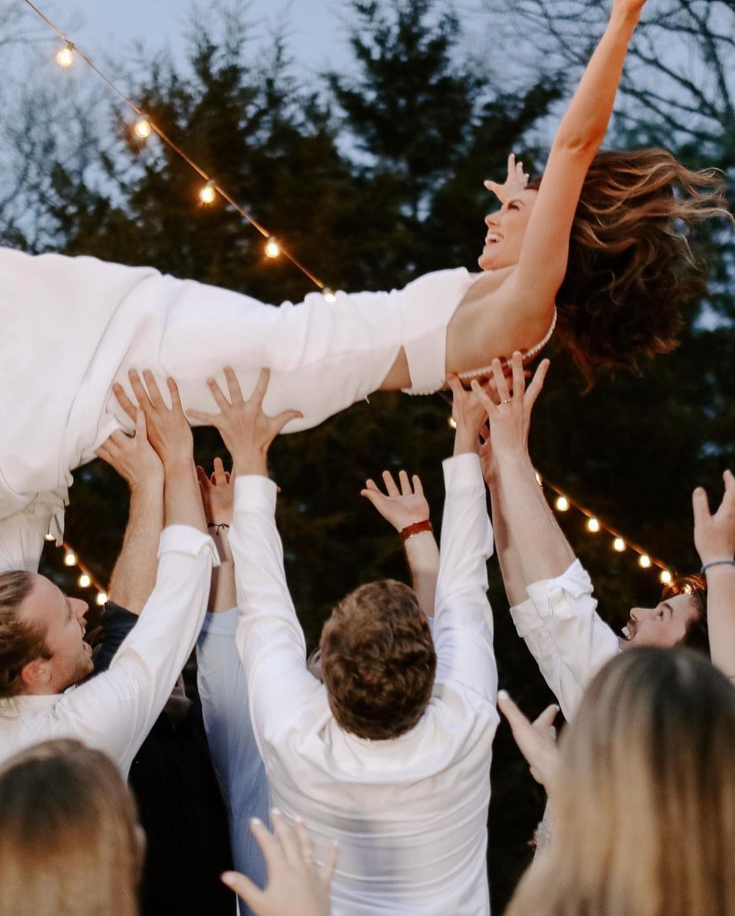 A bride crowd-surfing over her guests under string lights